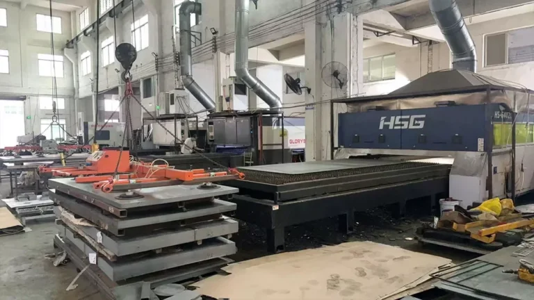 Large HSG laser cutting machine in an industrial factory with metal sheets and a lifting crane overhead.